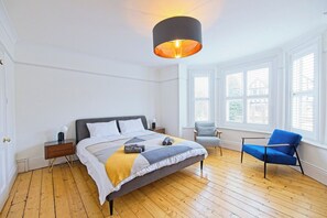 Ein Schlafzimmer mit einem Bett, einem Nachttisch, einem Sessel und einem Fenster mit Jalousien.