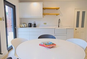 A compact kitchen with white cabinets, a sink, and a small countertop. There is a table with two chairs and a book on it.