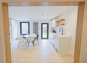 Una cocina moderna con armarios blancos, encimera de madera y una zona de comedor con mesa y sillas blancas.