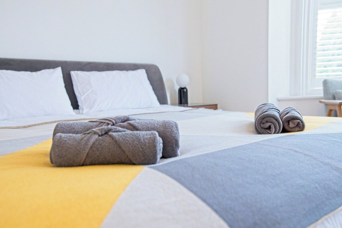 Un lit bien fait, recouvert d’une couverture grise et jaune, avec un oreiller gris et des serviettes grises pliées posées sur le lit.