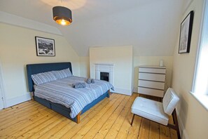 Ein Schlafzimmer mit einem Bett, einem weißen Sessel, einem Kamin und einem Bild an der Wand.