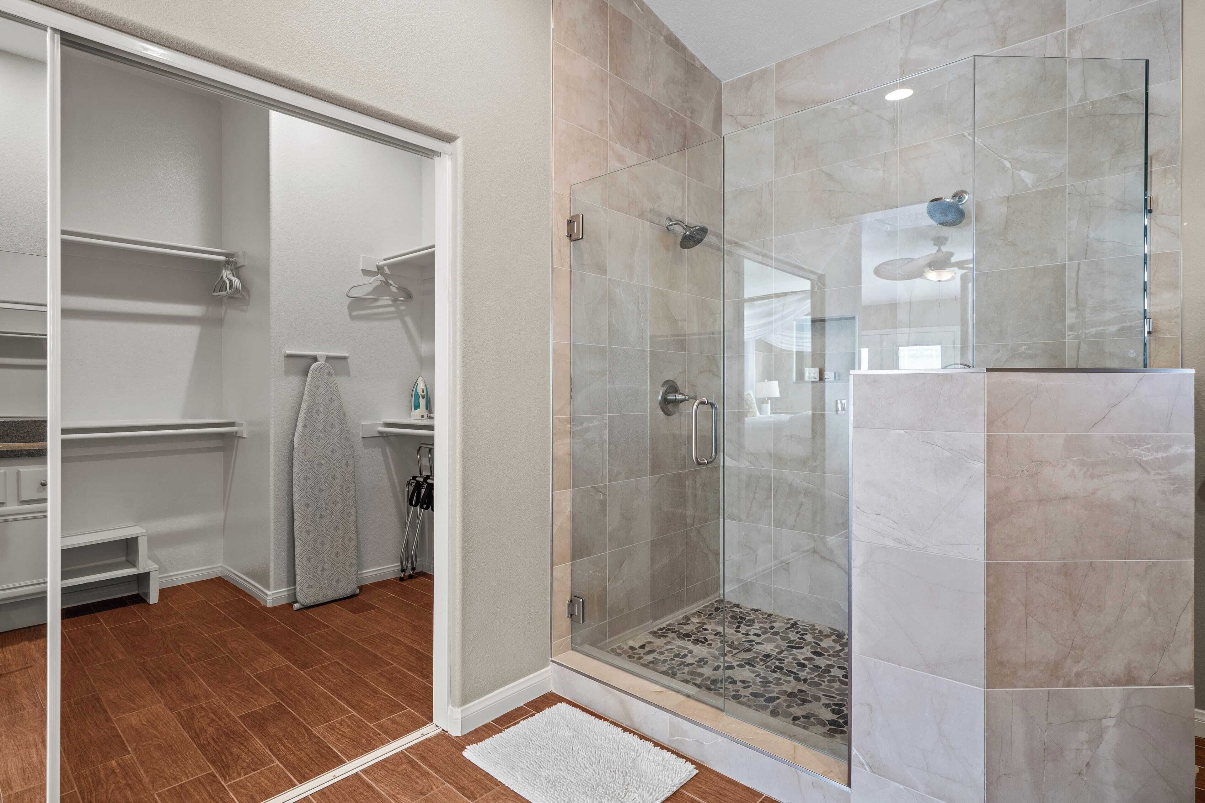Une salle de bain moderne avec une douche à parois de verre, un dressing et un tapis blanc.