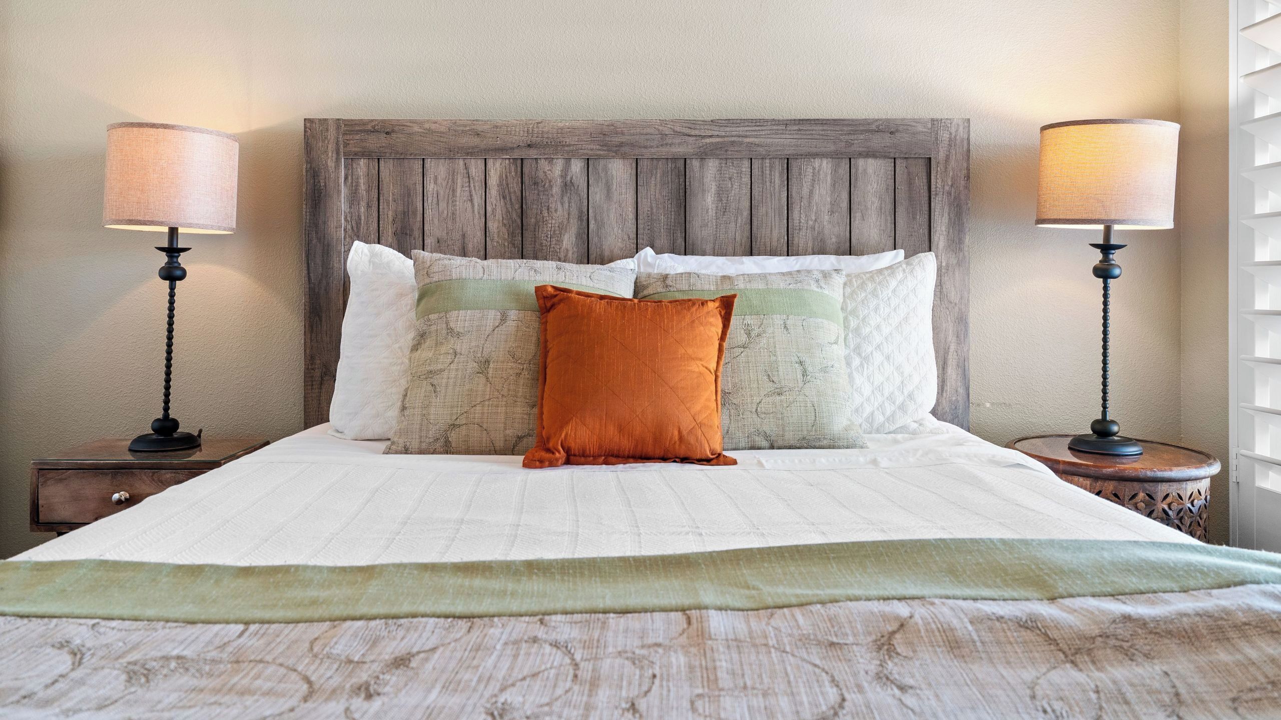 A neatly made bed with a wooden headboard, multiple pillows, and two bedside lamps.