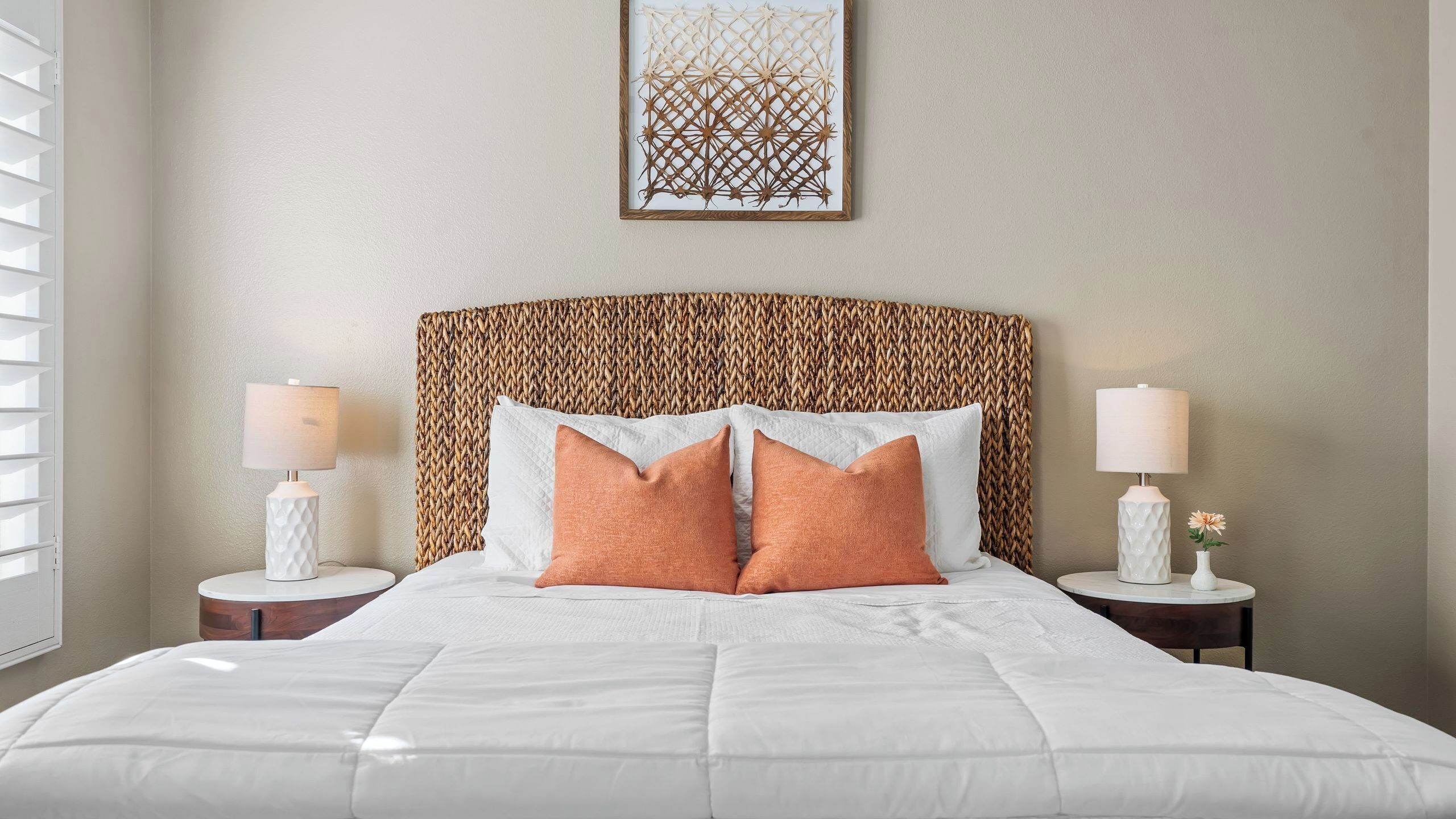 A neatly made bed with white bedding, two bedside tables with lamps, and a woven headboard.