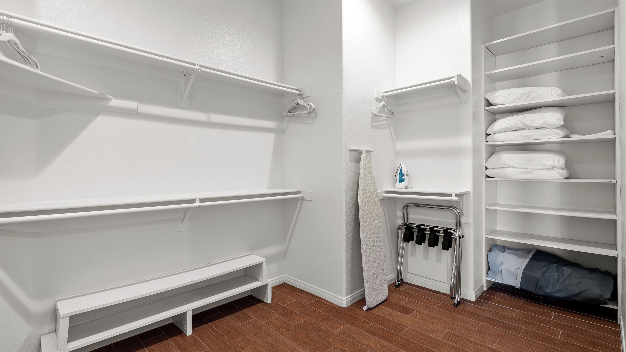 Un placard blanc avec des étagères, un banc et un porte-vêtements.