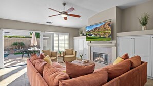 A living room with a sofa, chairs, a TV, a fireplace, and a ceiling fan.