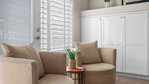 A room with a beige sofa, a small side table with a plant, and a white wardrobe.