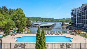 Un espace piscine avec des chaises longues et une vue sur un lac et des bâtiments.