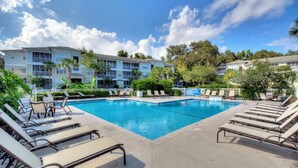 A pool area with lounge chairs and a building in the background. - Beautifully Decorated Condo, St. Simons Island, 8 minutes to Beach, Heated Pool (St. Simons Island)