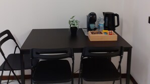 A dining area with a table, chairs, a coffee maker, a kettle, and a small plant.