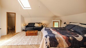 Une chambre avec un grand lit, un canapé, une commode en bois, un tapis à motifs et des fenêtres de toit.