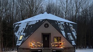 Une cabane dont le toit est recouvert de neige, une véranda à l’avant ornée de guirlandes lumineuses et une table de pique-nique devant.
