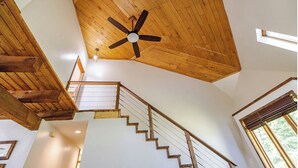 Un escalier en bois, un ventilateur de plafond, des murs blancs et une fenêtre avec des stores.