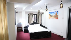 A hotel room with a large bed, a TV, a desk, and a painting on the wall.