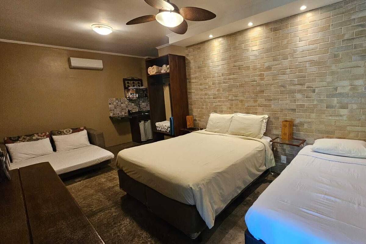 Une chambre d’hôtel avec un grand lit, un lit plus petit, un bureau, une chaise, une armoire et un mur en briques.