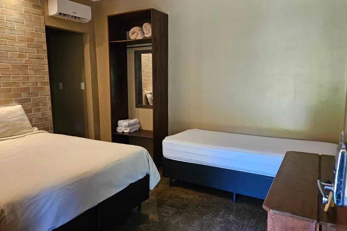 Une chambre d’hôtel avec un lit, une banquette, une petite table et un climatiseur fixé au mur.