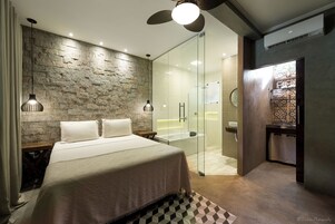 Quarto moderno com parede de pedra, chuveiro de vidro e um banco de madeira.