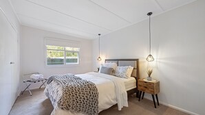 A bedroom with a bed, bedside table, lamp, and a window with a view of greenery. - Paradise Retreat Lakehouse  - Jamieson - Sleeps 10 (Jamieson)