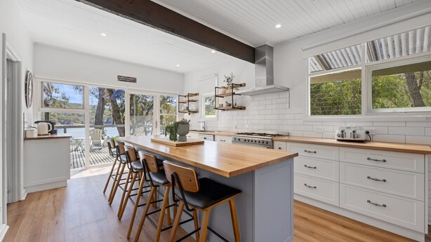 A modern kitchen with a large island, bar stools, white cabinetry, and a view of the outdoors. - Paradise Retreat Lakehouse  - Jamieson - Sleeps 10 (Jamieson)