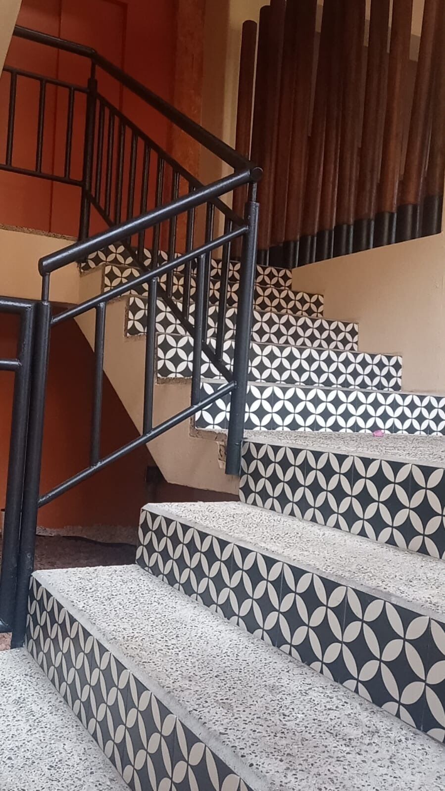 Una escalera con un patrón geométrico de azulejos, barandilla de metal y panel de pared de madera.
