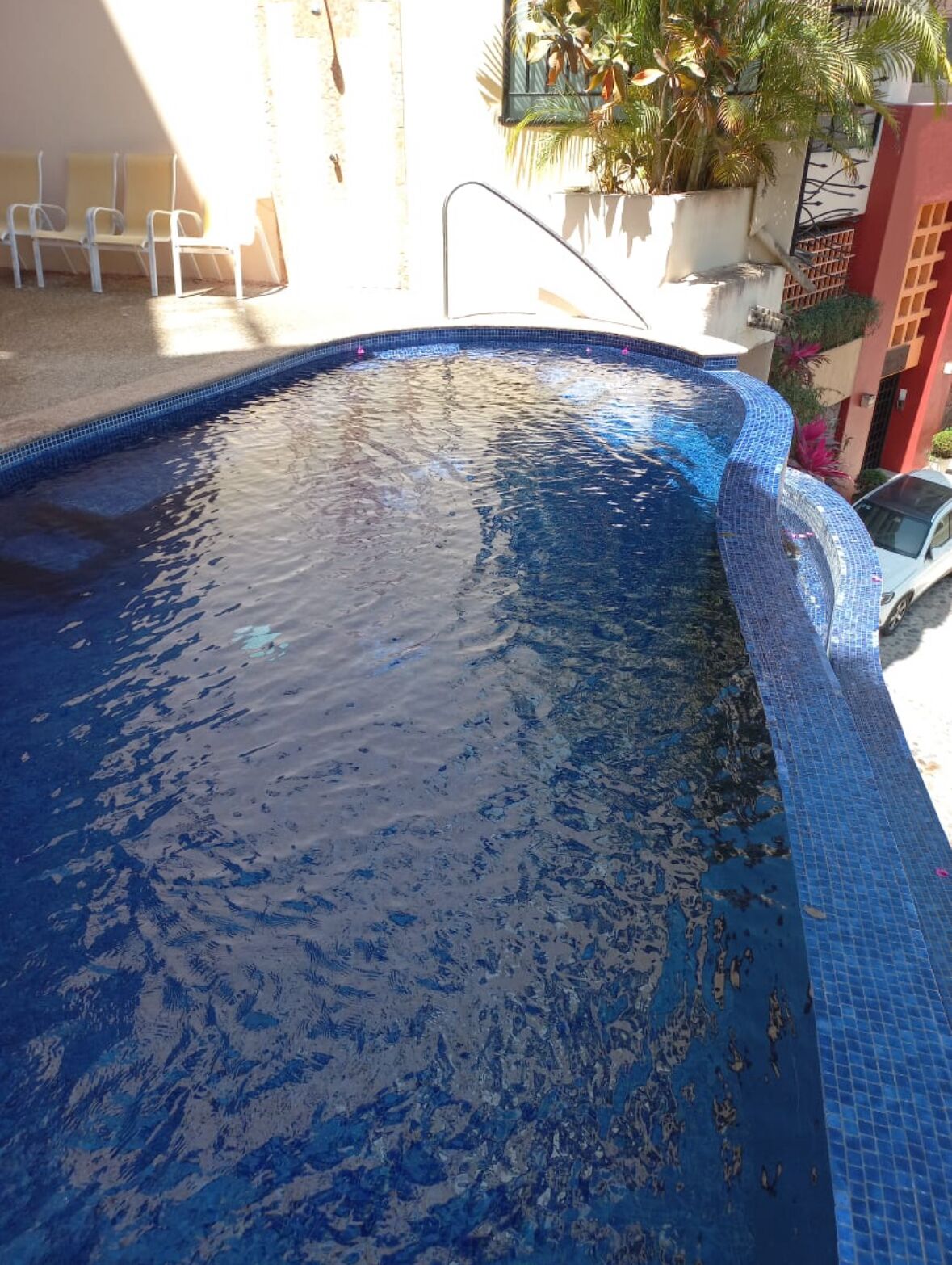 A swimming pool with a tiled edge and a few chairs nearby.