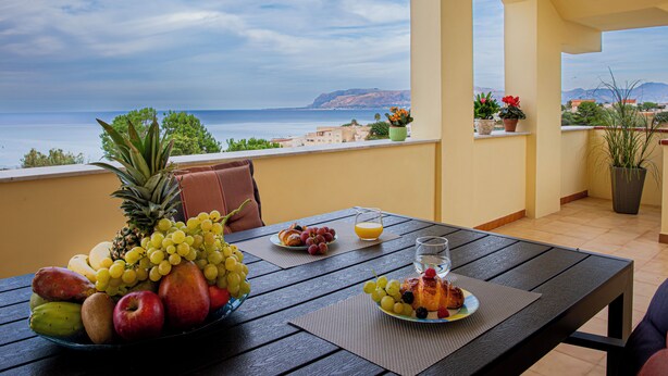 A table with fruits, a glass of water, and a plate with pastries, overlooking a scenic view of the sea and mountains. - Star Apartment, Alcamo Marina, 3 bedrooms, swimming pool, view and fun... enjoy (Alcamo)
