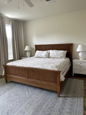 A bedroom with a wooden bed, white bedding, two bedside lamps, a window with curtains, and a patterned rug.