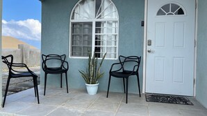Une maison avec une porte blanche, une grande fenêtre en arc de cercle et deux chaises noires à l’extérieur.