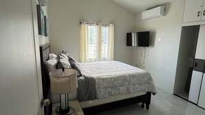 Une chambre à coucher comprenant un lit, une table de chevet avec une lampe, un téléviseur fixé au mur et une armoire.