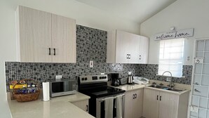 Une cuisine moderne avec des meubles en bois clair, un pare-feu en carreaux noirs, des appareils en acier inoxydable et une fenêtre avec des stores.