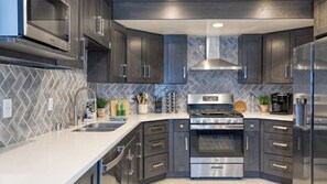 Une cuisine moderne avec des meubles de couleur sombre, des appareils en acier inoxydable et un dosseret de carreaux disposés en motif chevron.