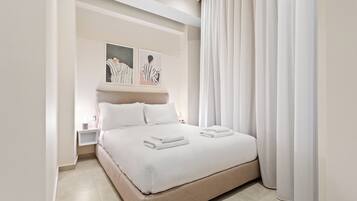 Une chambre d’hôtel moderne avec un grand lit, du linge de lit blanc, une table de chevet et des œuvres d’art accrochées au mur.