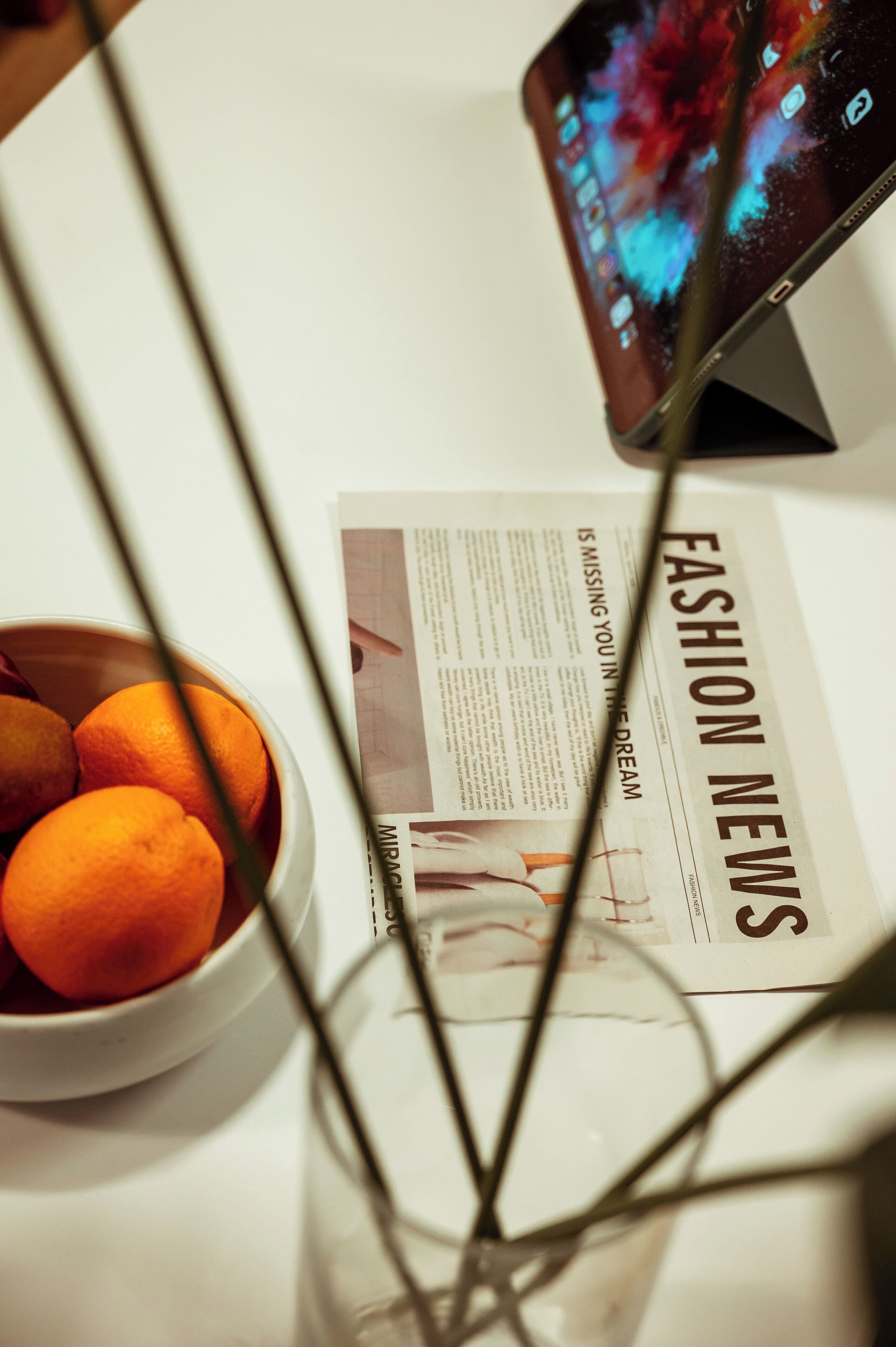 Una mesa con un bol de naranjas, un periódico y un teléfono inteligente mostrando contenido de colores.