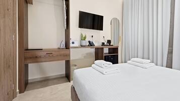 A modern hotel room with a wooden desk, a flat-screen TV, a bedside table with a lamp, and a bed with neatly folded towels.