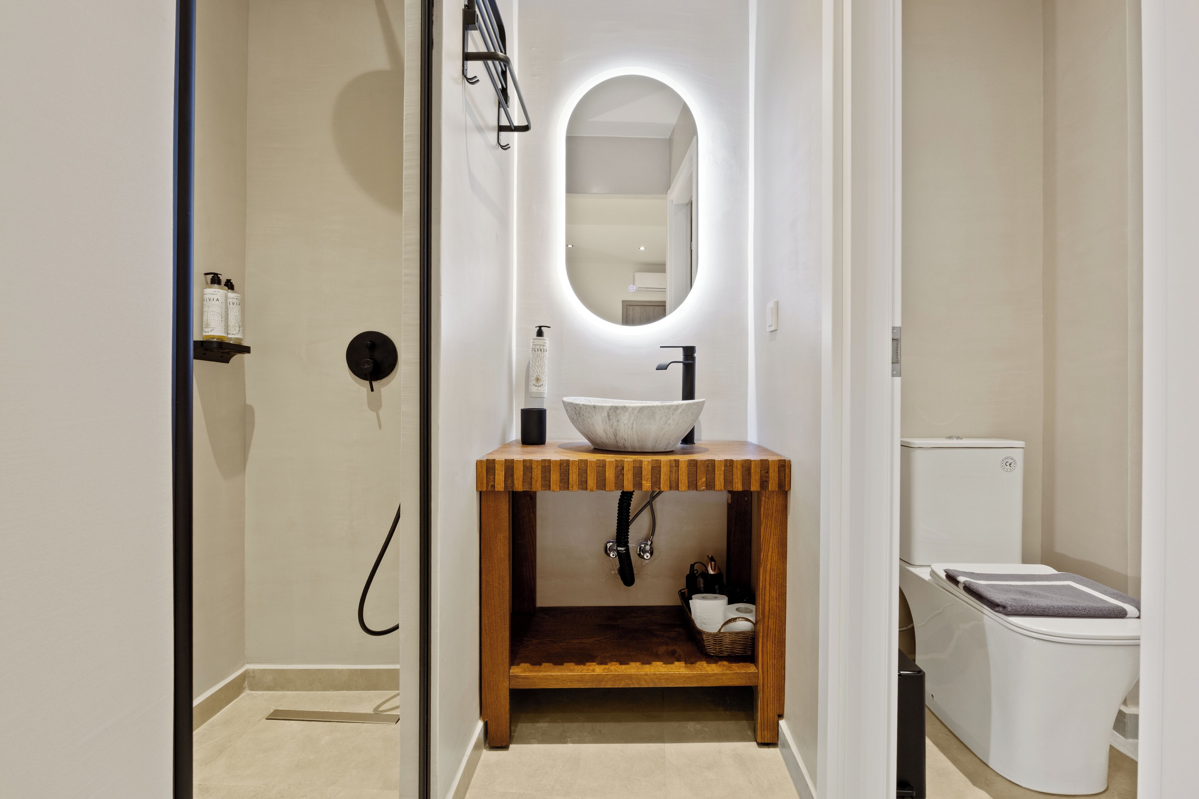 A modern bathroom with a wooden vanity, a large oval mirror, and a white toilet.