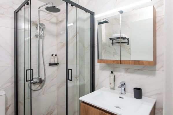 Une salle de bain moderne avec une douche à parois de verre, un lavabo blanc et un miroir au-dessus du lavabo.