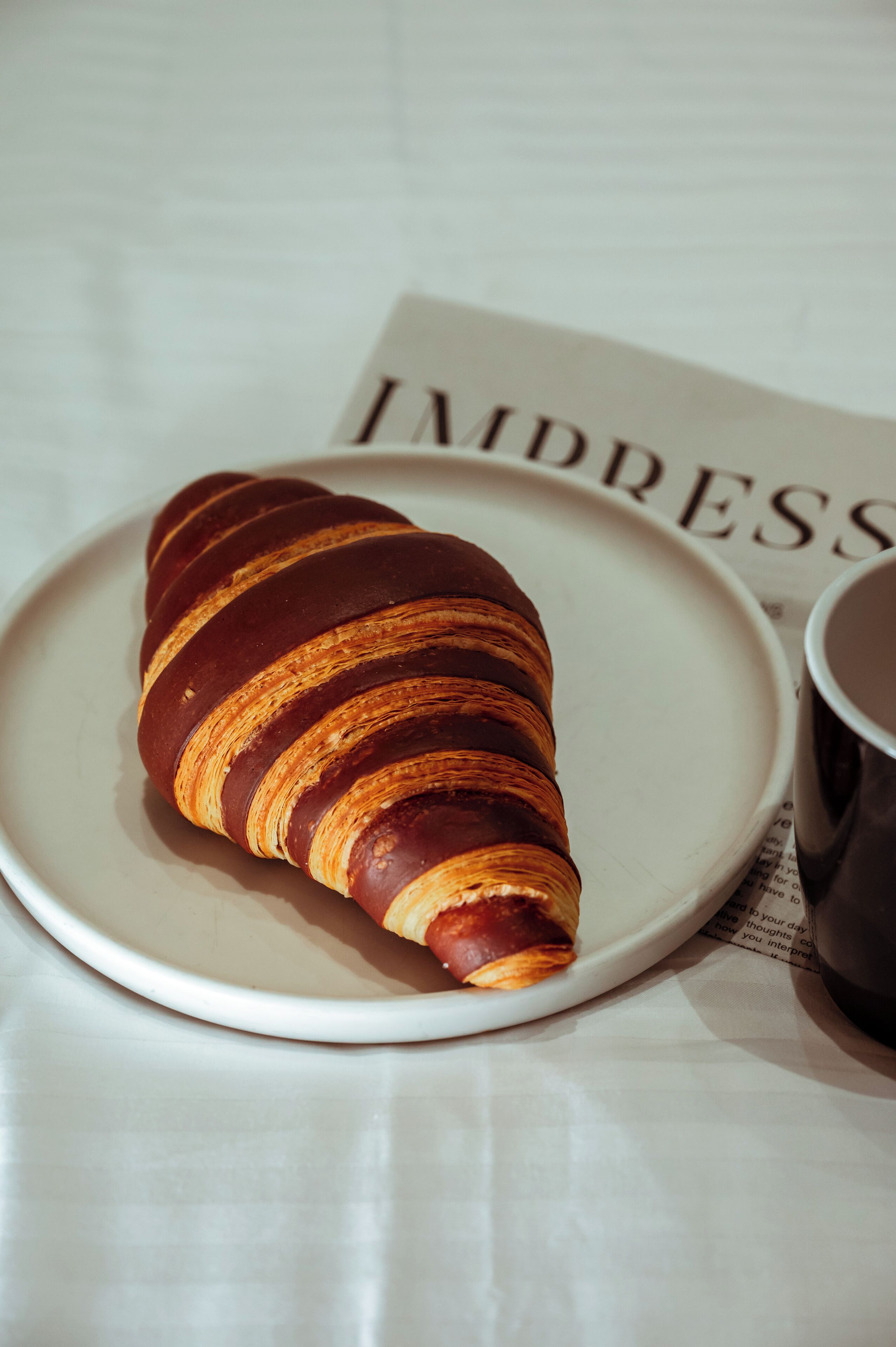Un croissant sur une assiette, accompagné d’une tasse et d’un menu.