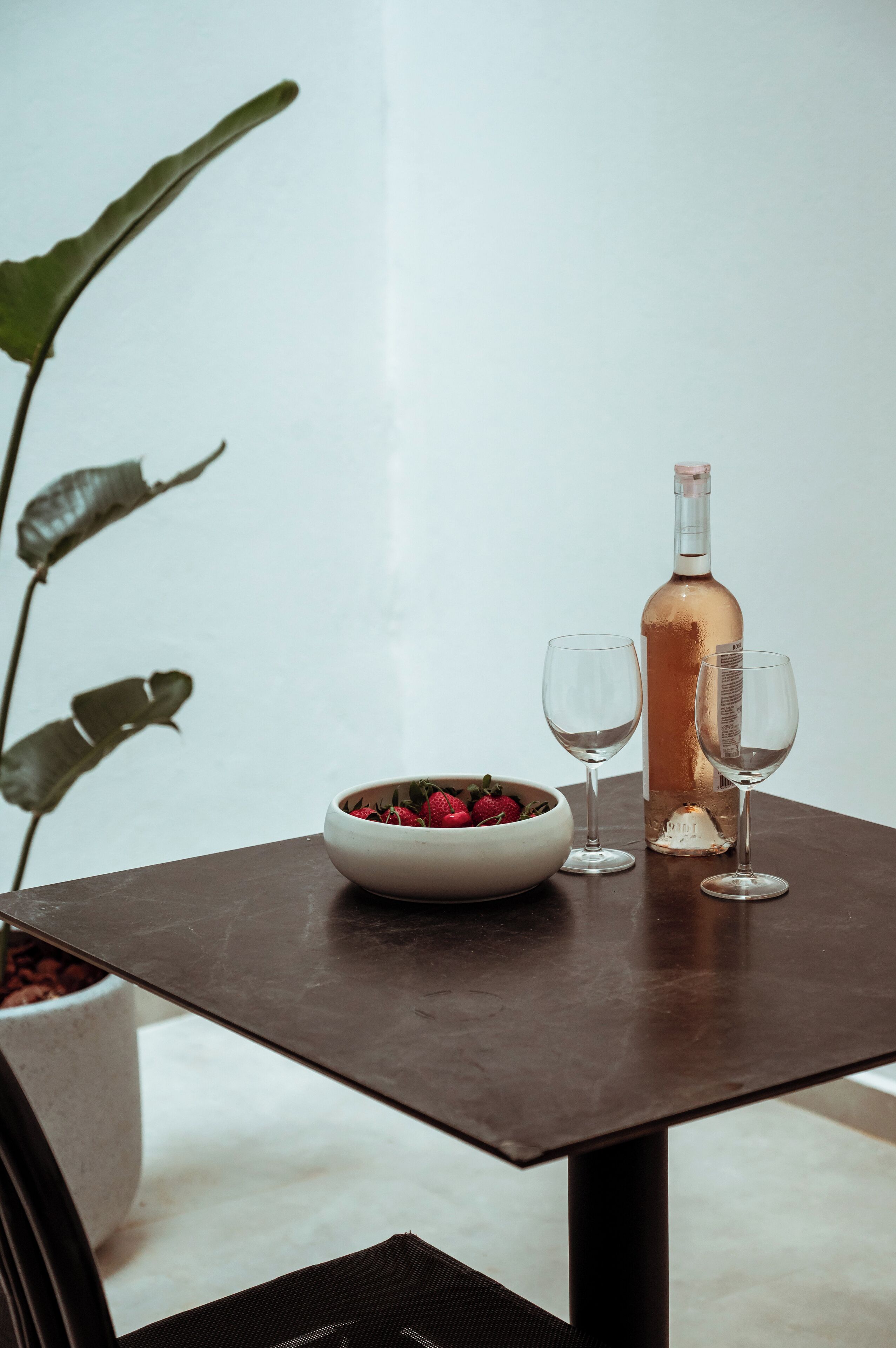 A table with a bowl of strawberries, a bottle of rosé wine, and two empty wine glasses.