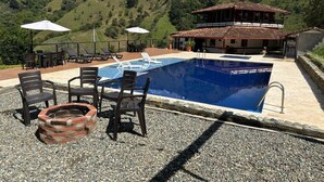 A swimming pool with lounge chairs and umbrellas, surrounded by a patio area with a view of green hills. - VILLA CATALINA FARM WITH SWIMMING POOL AND JACUZZI NEAR LA PINTADA  (Santa Bárbara)