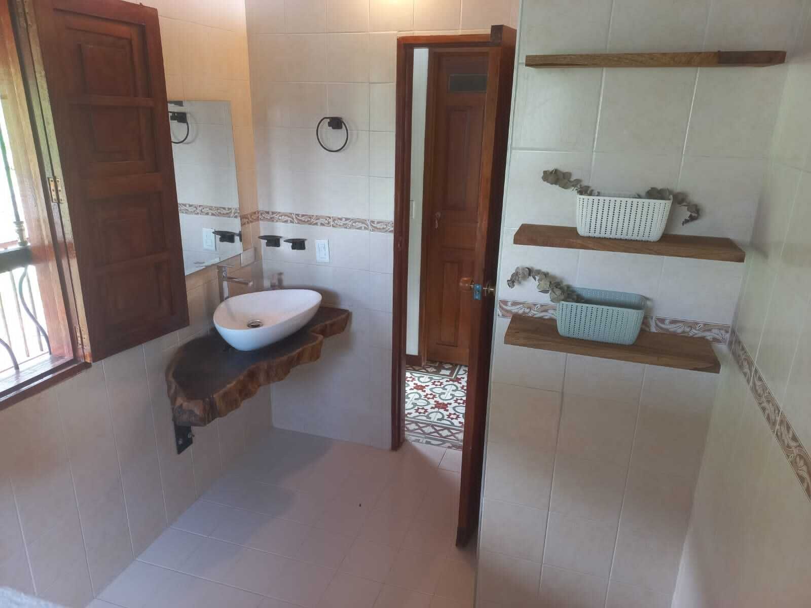 Une salle de bain avec un lavabo blanc, des étagères en bois et un carrelage à motifs.