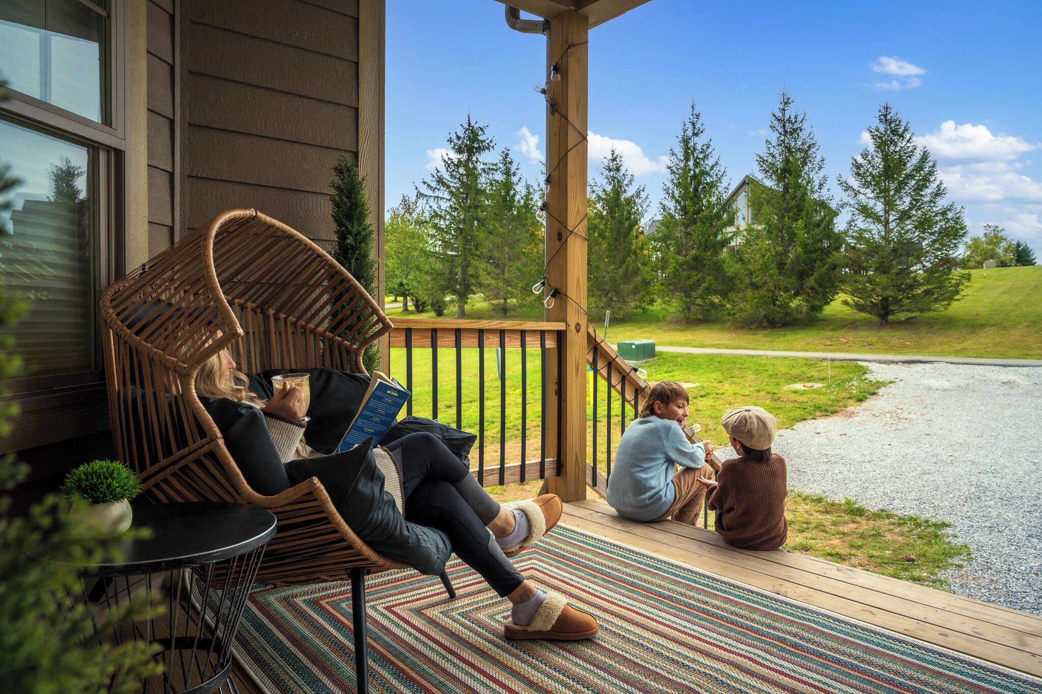 A wooden deck with wicker chairs and a small table, overlooking a grassy area with trees.