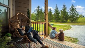 A wooden deck with wicker chairs and a small table, overlooking a grassy area with trees.