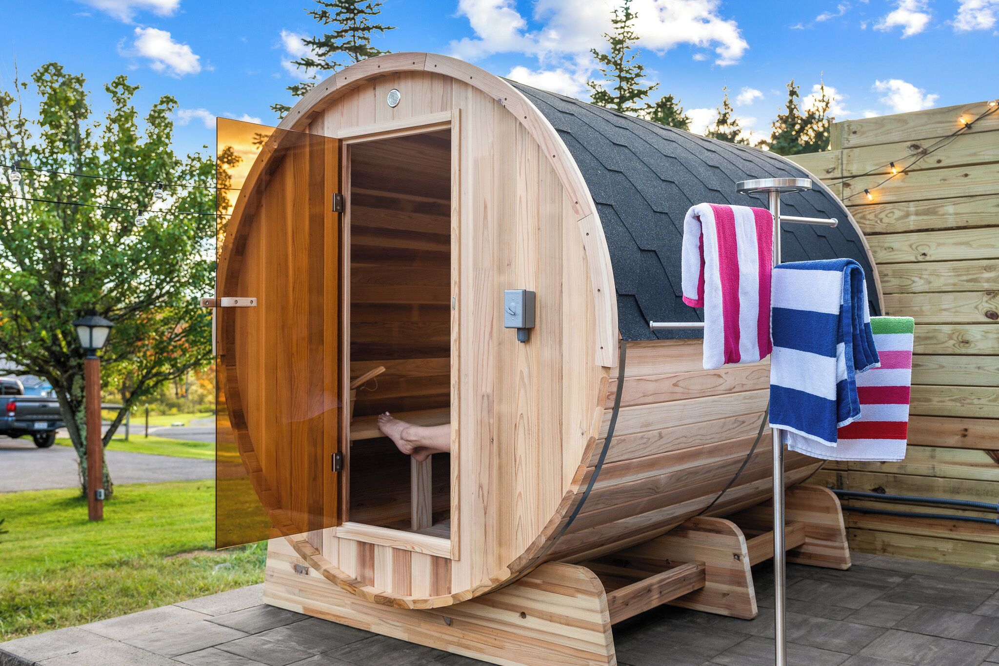 A wooden sauna with a curved exterior, a door, and a towel rack with striped towels.