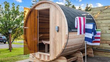 A wooden sauna with a curved exterior, a door, and a towel rack with striped towels.