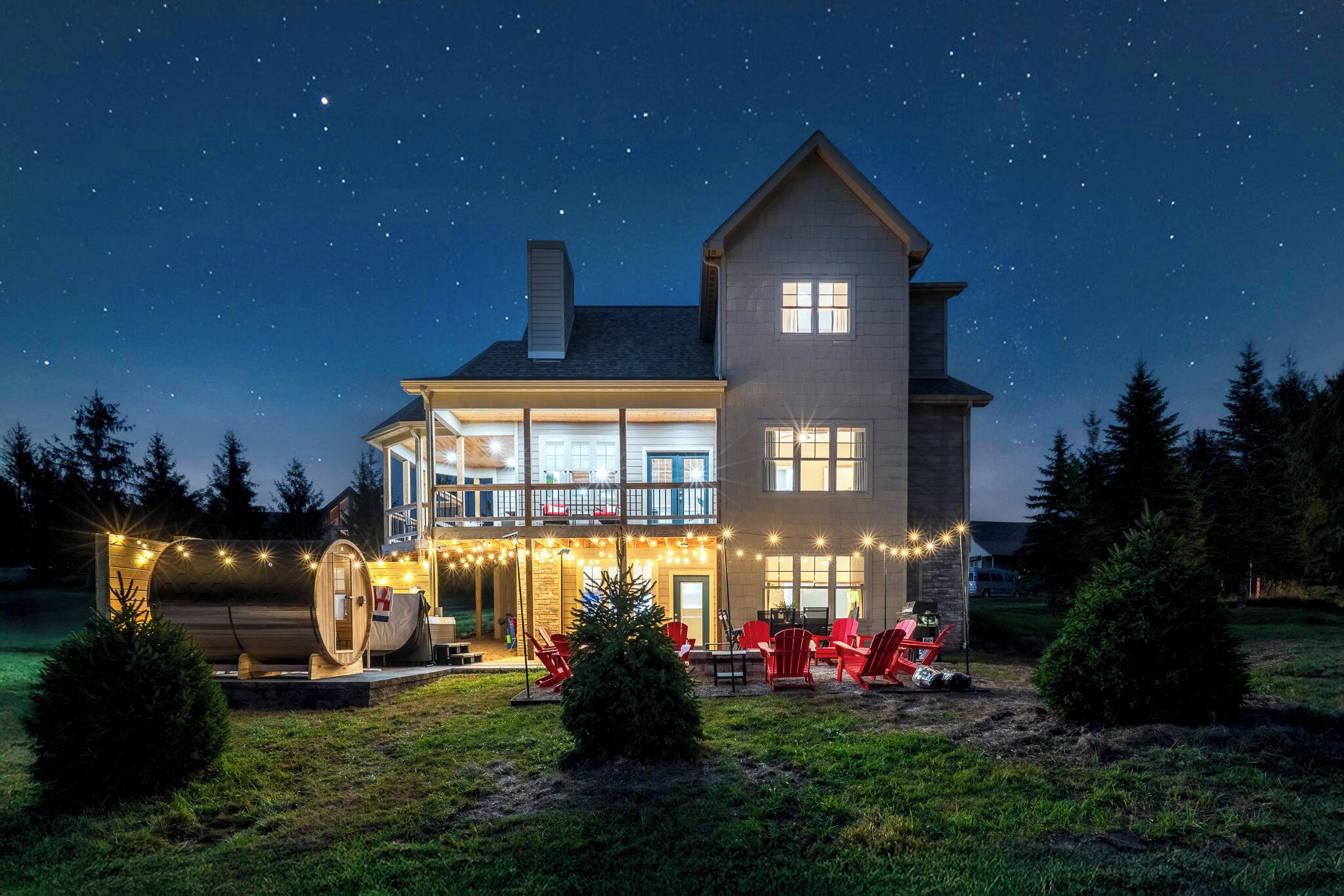 A two-story house with a balcony, outdoor seating, and string lights.