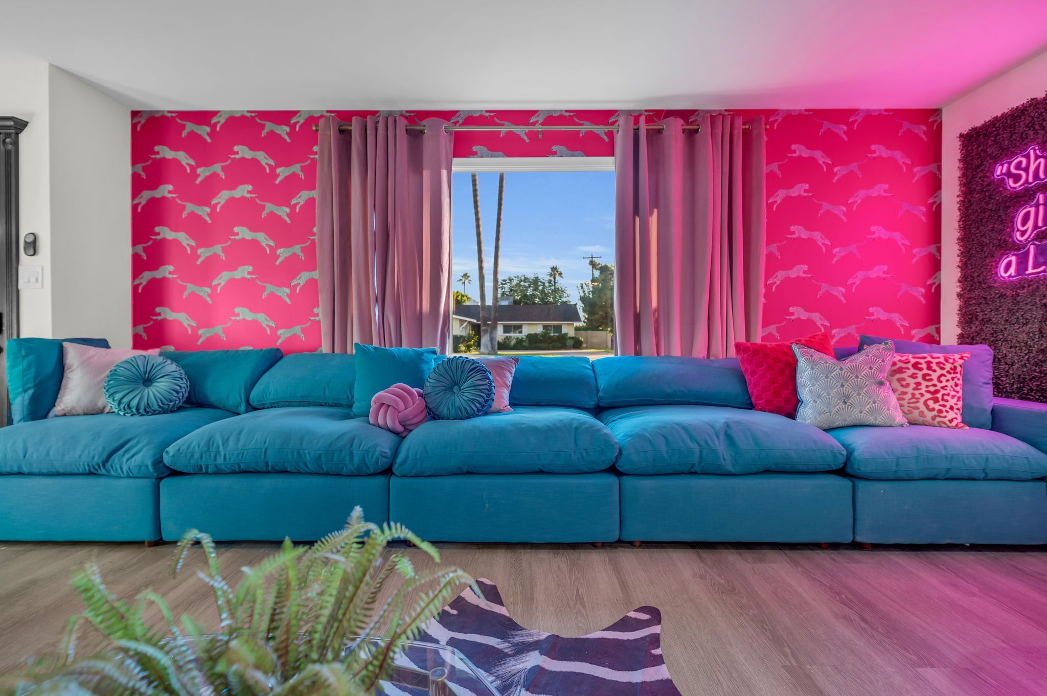 A teal sectional sofa with multiple pillows, a wooden floor, and a pink wall with a pattern.
