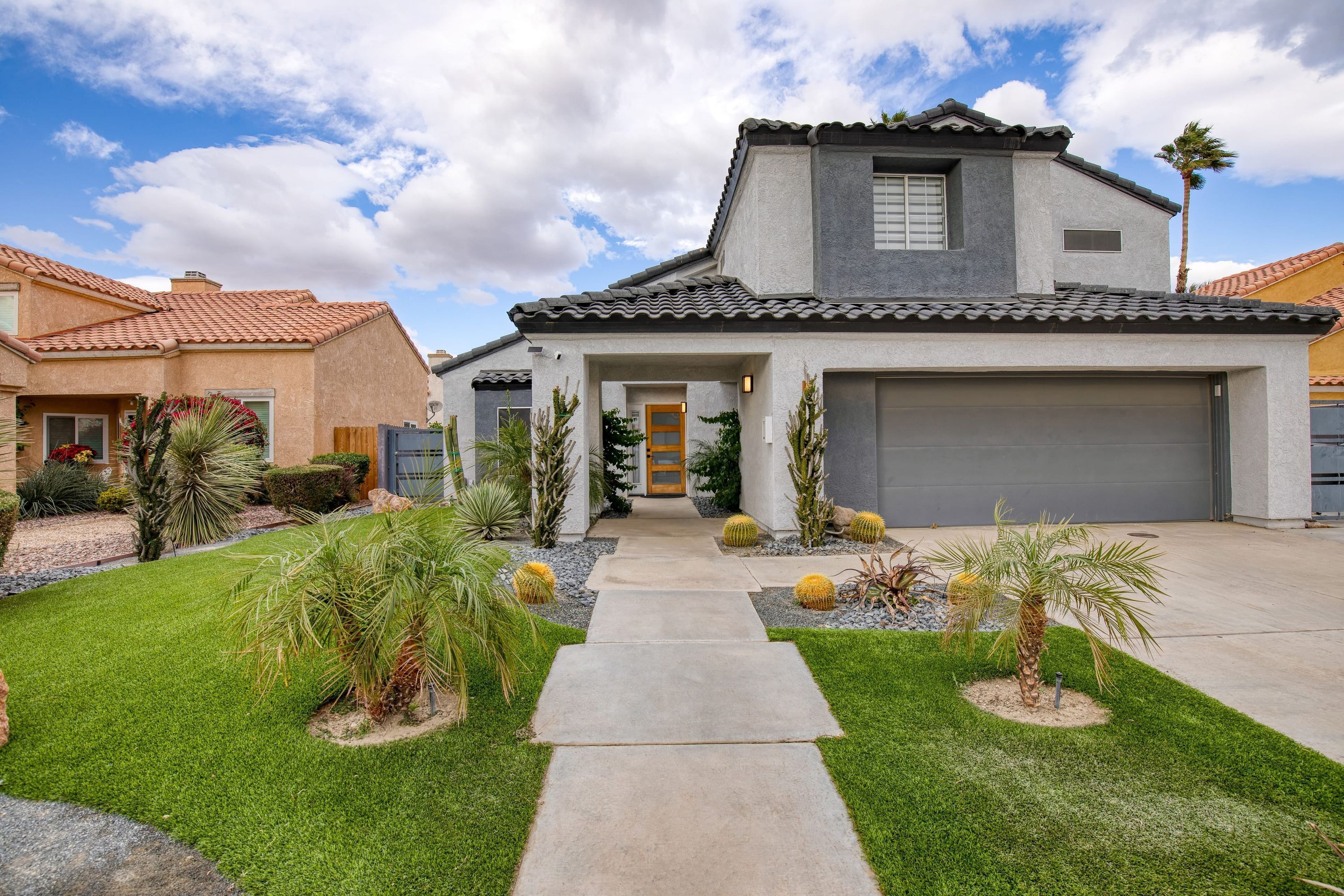 A modern two-story house with a front garage, a well-maintained lawn, and a variety of desert plants.