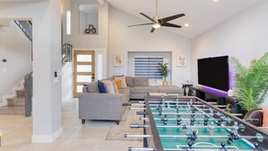 A spacious living room with a foosball table, a sofa, a television, and a ceiling fan. - Desert Scarif Private Pool Hot Tub Putting Green Near Coachella Festivals (Indio)