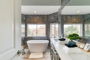 Une salle de bain moderne avec une baignoire sur pieds, de grandes fenêtres et un pare-baignoire en marbre.