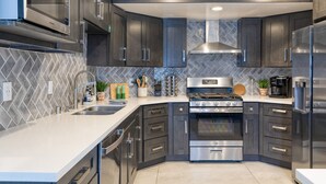 A modern kitchen with dark cabinetry, stainless steel appliances, and a herringbone tile backsplash. - Desert Scarif Private Pool Hot Tub Putting Green Near Coachella Festivals (Indio)